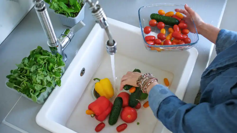 Woman washing vegetables under the new chrome kitchen faucet.